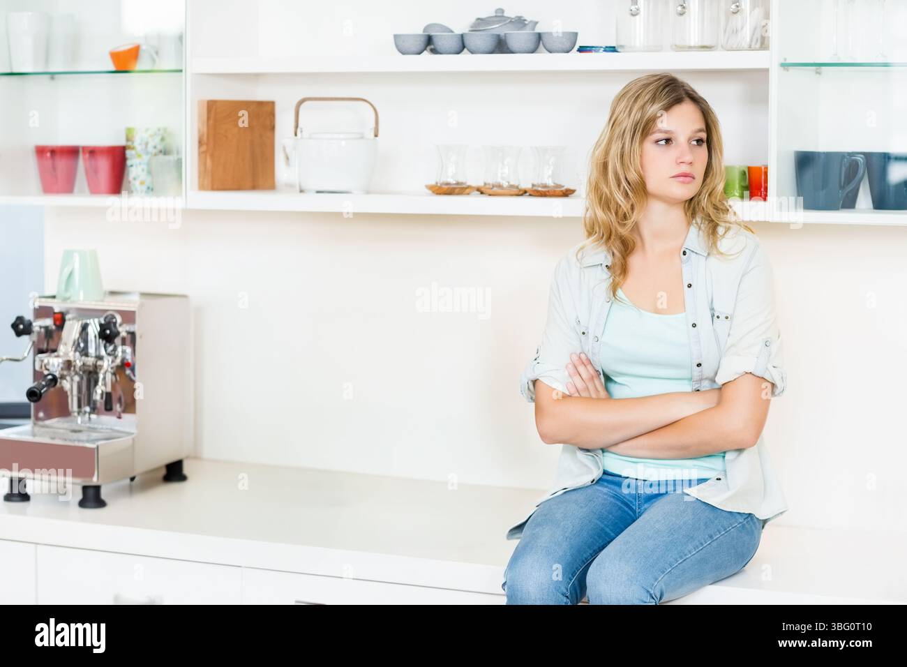 Frau, die auf weißer Arbeitsplatte in der Küche neben Edelstahl-Espresso-Maschine sitzt, Kopierraum Stockfoto