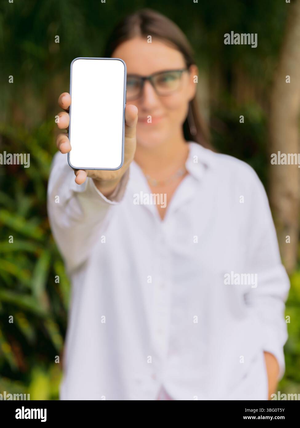 Lächelnde Frau zeigt ein Smartphone mit leerem Bildschirm draußen. Mockup für App-, Website- oder Social-Media-Design. Stockfoto