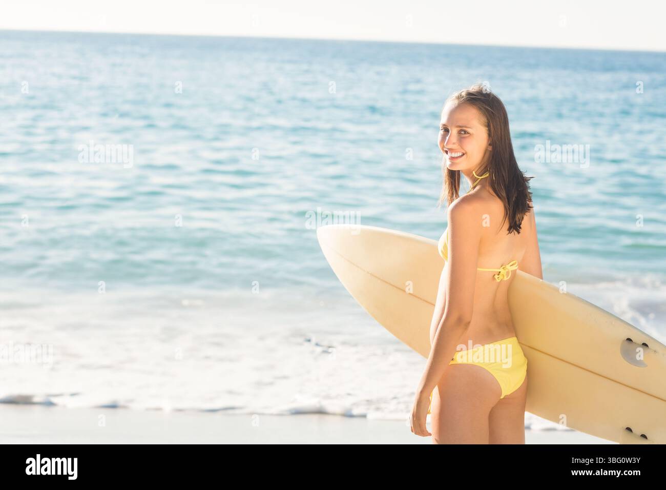 Surferin mit Surfbrett, Blick zurück zur Kamera am Strand in gelben Badeanzügen, Kopierraum Stockfoto