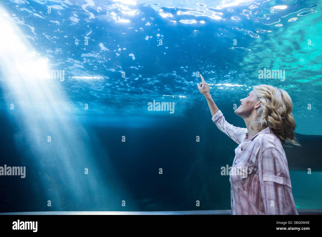 Lichtschäfte, die durch Aquarienglas in blau-grünem Wasser filtrieren und Gesteinssilhouetten freigeben Stockfoto