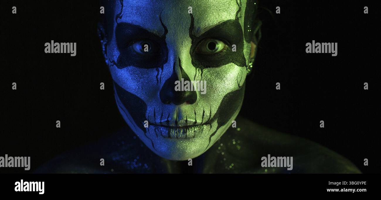 Isoliert auf schwarzem Großbild-Nahaufnahme, grün und blau getönt, schöne gruselige junge blonde weiße Frau mit Schädelkörperkunst, graue Augen, pe Stockfoto