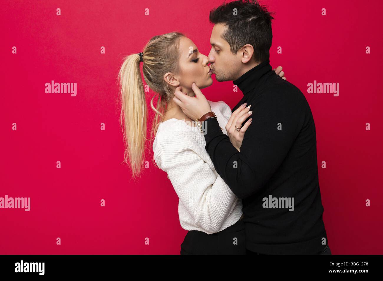 Foto eines schönen jungen blonden weißen Strickpullovers und eines erwachsenen Brunet-Mannes mit Stoppeln in einem schwarzen Pullover, der sich isoliert auf einem pi küsst Stockfoto