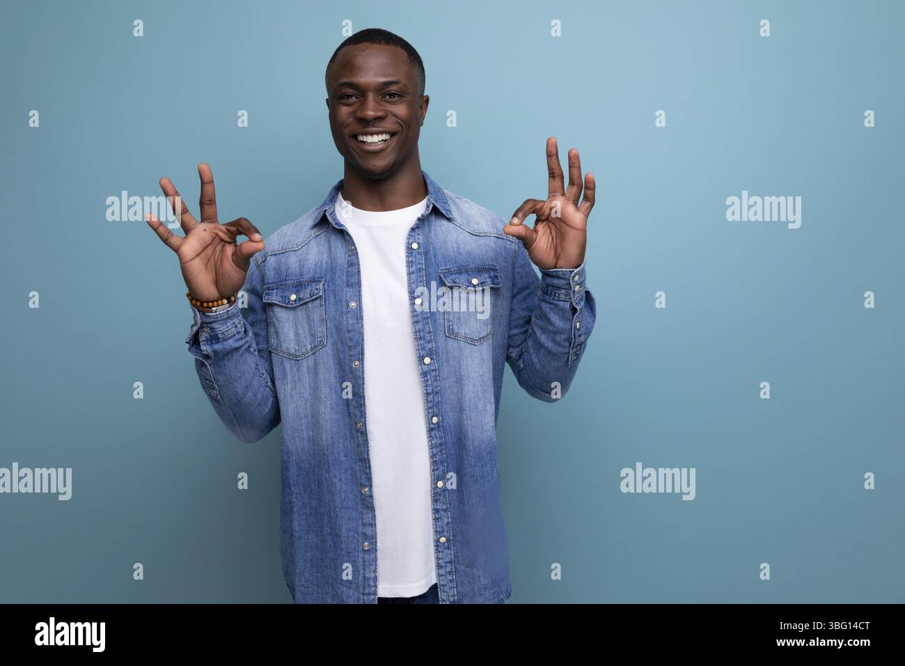 Junger energiegeladener positiver amerikanischer Mann mit dunkler Haut, der stilvoll in Jeans gekleidet ist und vor dem Hintergrund mit Kopierraum lächelt Stockfoto
