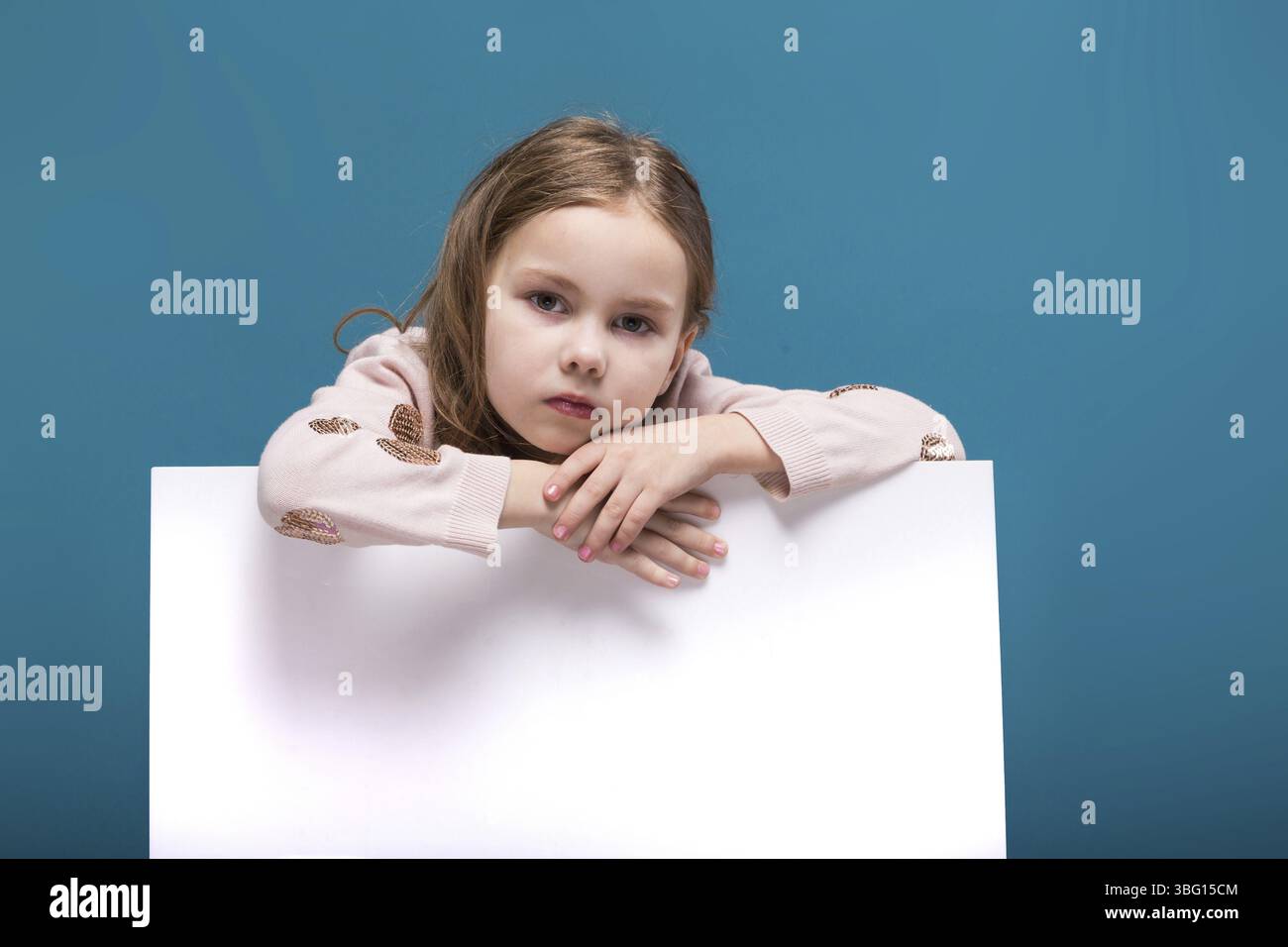 Isoliert auf blauem, attraktivem weißbrünetten Kind mit langen Haaren, in beigefarbenem Mantel und blauer Jeans zeigen leeres Poster, verlässt sich auf das Poster, schauen Sie sich ca. Stockfoto