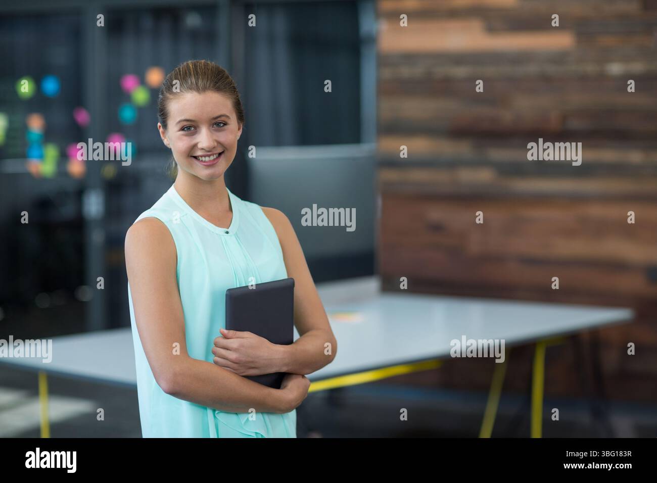 Tablette auf weißem Tisch mit gelben Beinen inmitten farbenfroher Haftnotizen im Großraumbüro Stockfoto