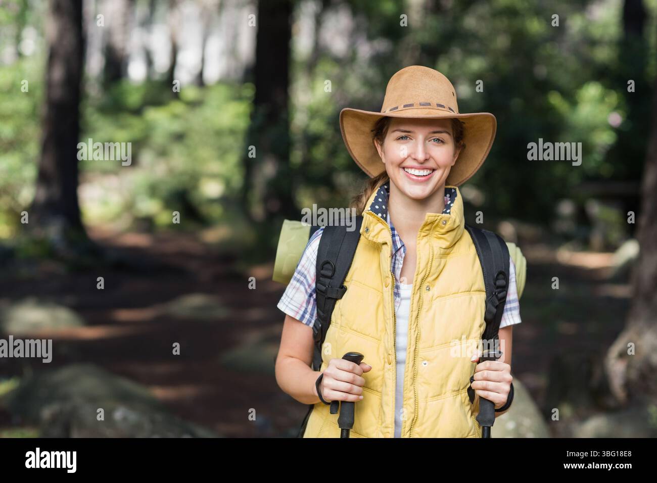 Wanderer, die auf bewaldeten Wegen steht, gelbe Weste trägt und Rucksack und Wanderstöcke trägt Stockfoto