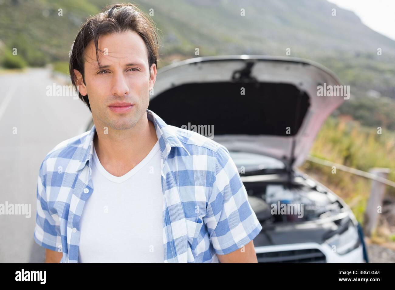 Mann mittleren Alters, der neben dem Fahrzeug mit offener Motorhaube auf Landstraßen steht und Motorkomponenten untersucht Stockfoto