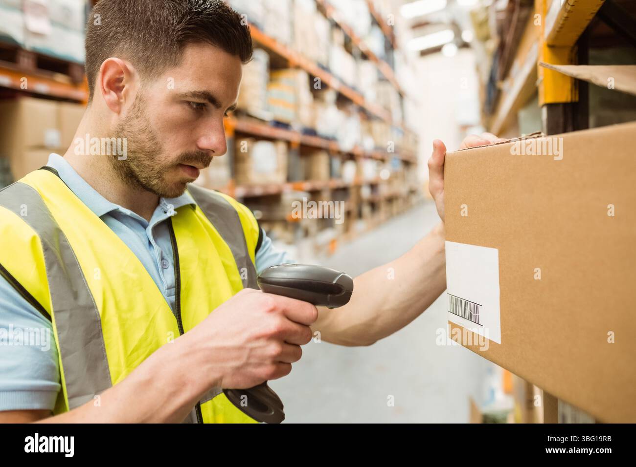 Männlicher Arbeiter mit Sicherheitsweste, der Barcode mit Scanner auf der Kiste im Lagergang scannt, Kopierraum Stockfoto