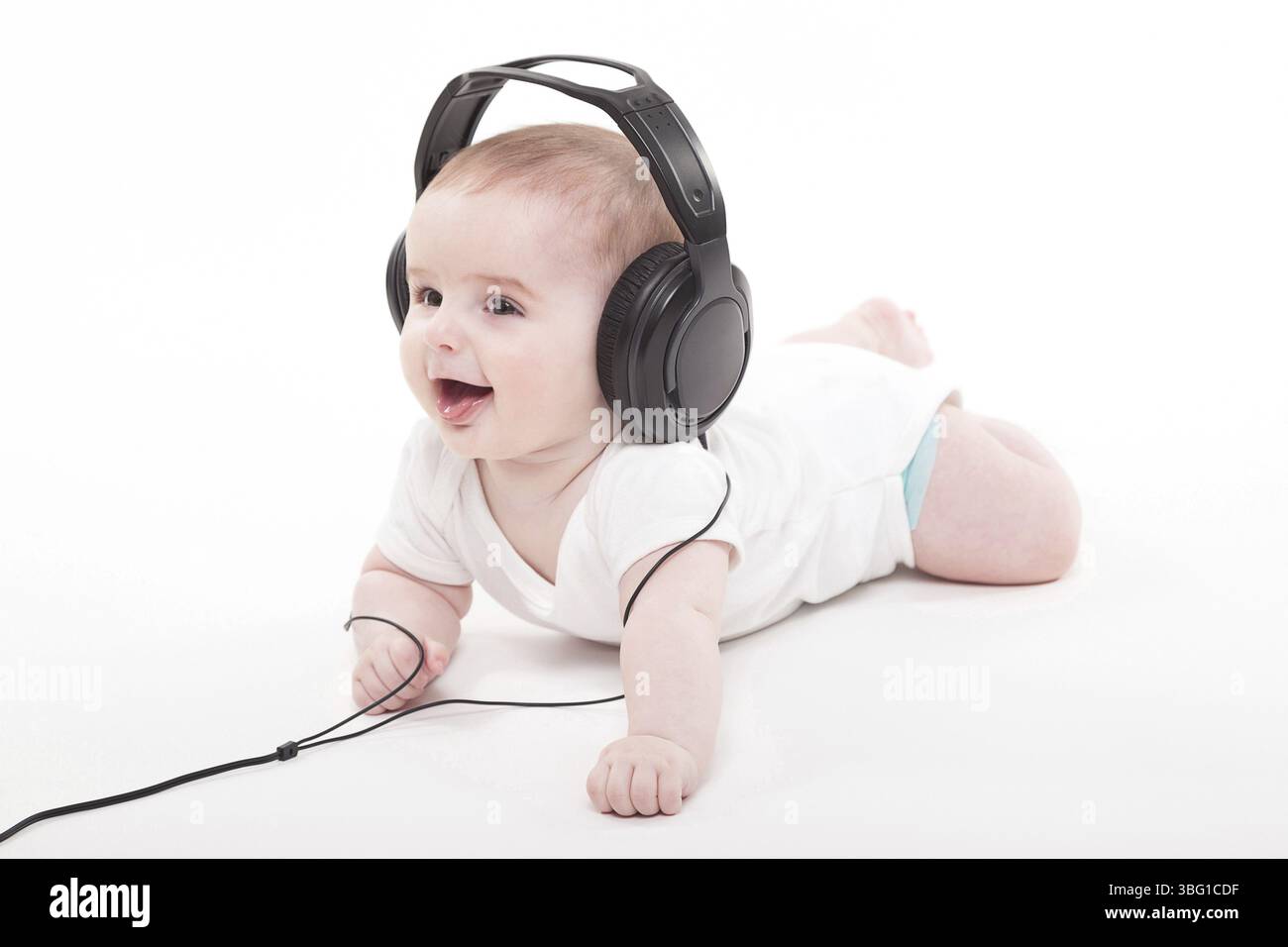 Bezauberndes Baby auf weißem Hintergrund mit Kopfhörern, die Musik hören. Foto aus der Schärfentiefe und künstlerischen Unschärfe Stockfoto