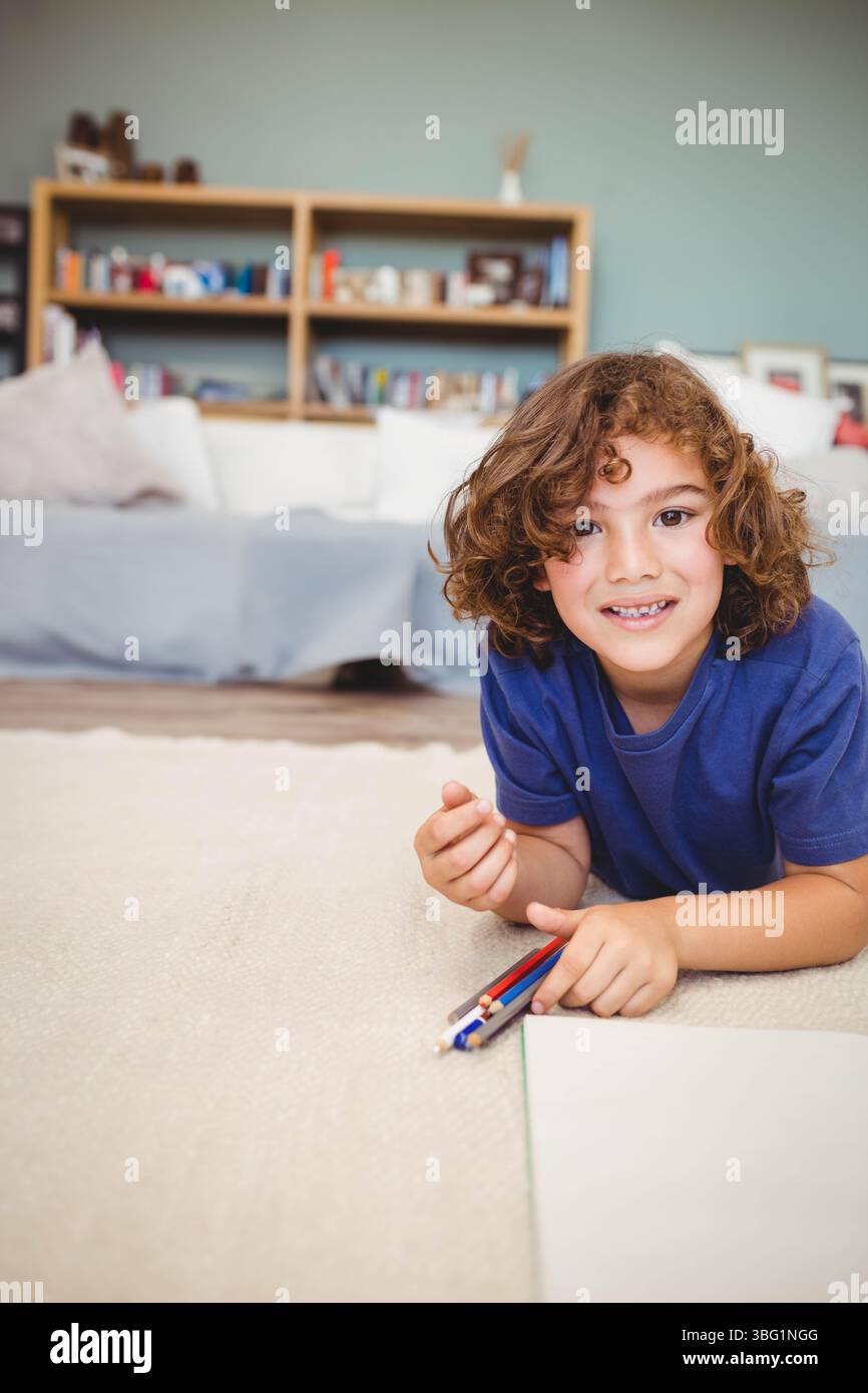 Farbstifte liegen auf beigefarbenem Teppich neben leerem Zeichenpapier bei Couch und hölzernem Bücherregal Stockfoto
