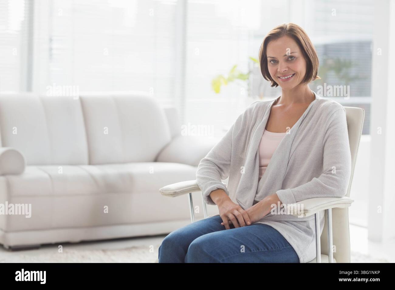 Gepolsterter Sessel mit hohen Fenstern, horizontalen Jalousien und grüner Pflanze im Wohnzimmer Stockfoto