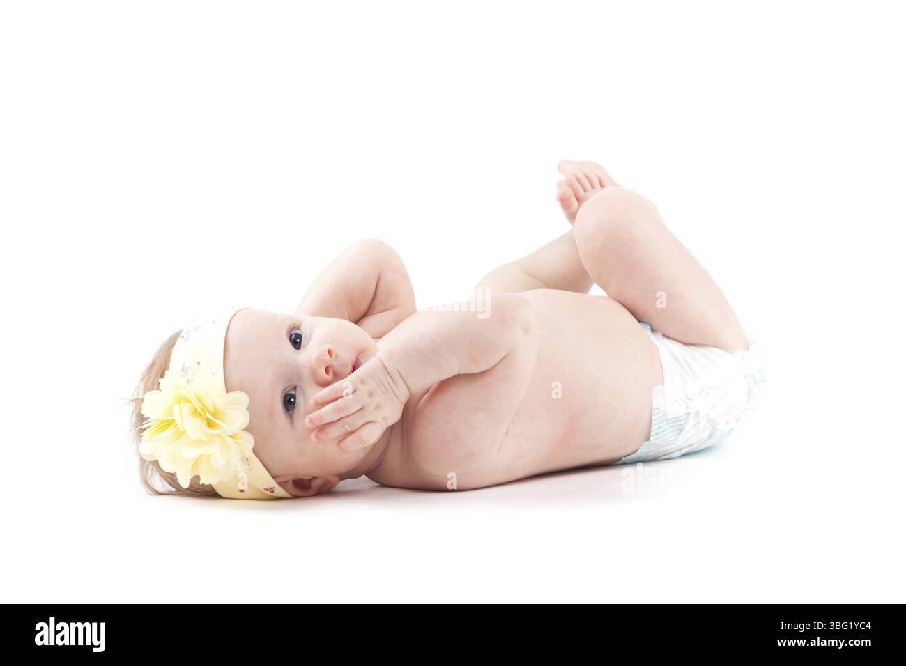 Isoliert auf weißem, süßem, staunendem weißem Baby Mädchen in Windel und weißem Kopf, gelbe Blumenverpackung liegt auf dem Rücken, Hände auf Gesicht Stockfoto