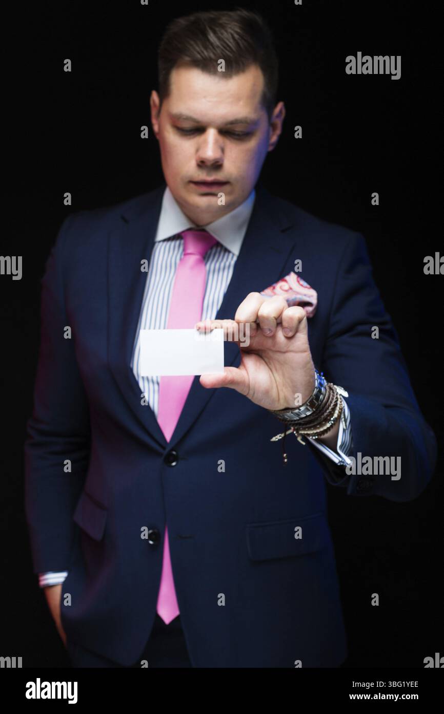 Junger kaukasischer eleganter, intelligenter und freundlicher Geschäftsmann ernsthaft durchdachter Mann in blauem Anzug, der im Büro steht und eine Telefonkonferenz-Karte anbietet Stockfoto