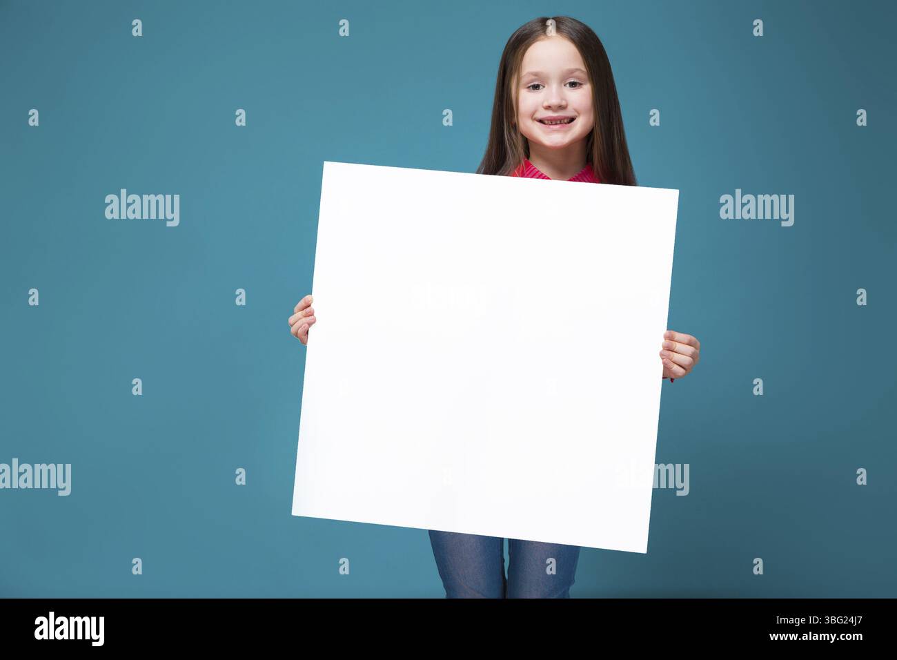 Isoliert auf blauem, wunderschönem weißbrünetten Kind in rotem kariertem Hemd und blauer Jeans mit langen Haaren halten leeres Poster, schauen Sie in die Kamera, stehen Sie dahinter Stockfoto