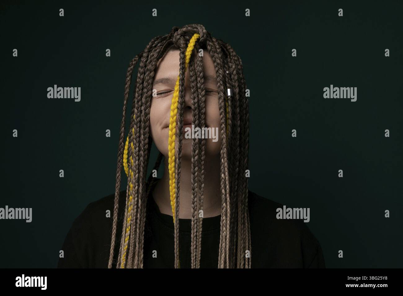 Eine Frau mit langen Dreadlocks steht vor einem leuchtend grünen Hintergrund. Ihr Haar kaskadiert ihren Rücken hinunter, während sie selbstbewusst für die Kommen posiert Stockfoto