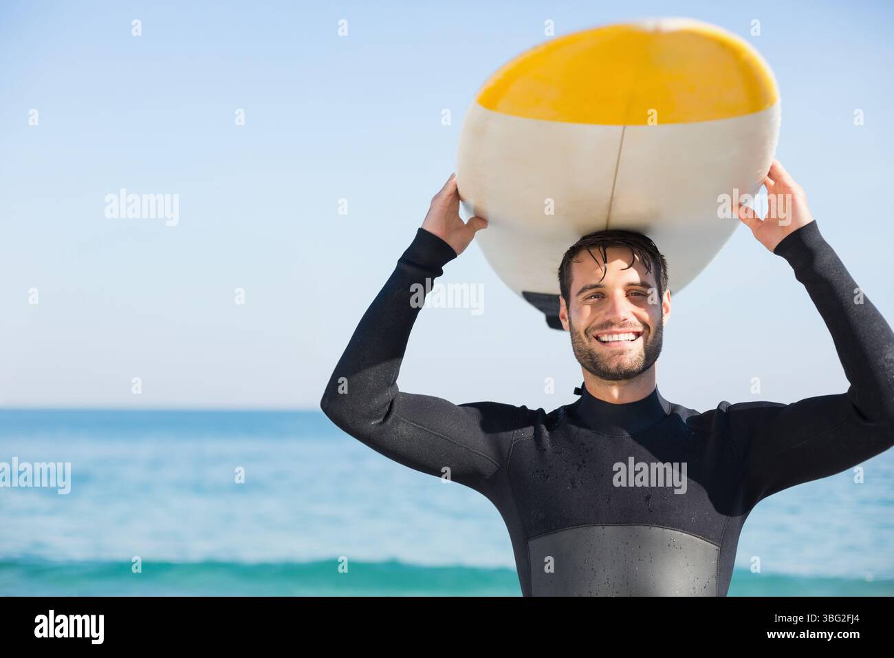 Männlicher Surfer in schwarzem Neoprenanzug mit Surfbrett mit gelber Nase und weißer Unterseite am Strand Stockfoto