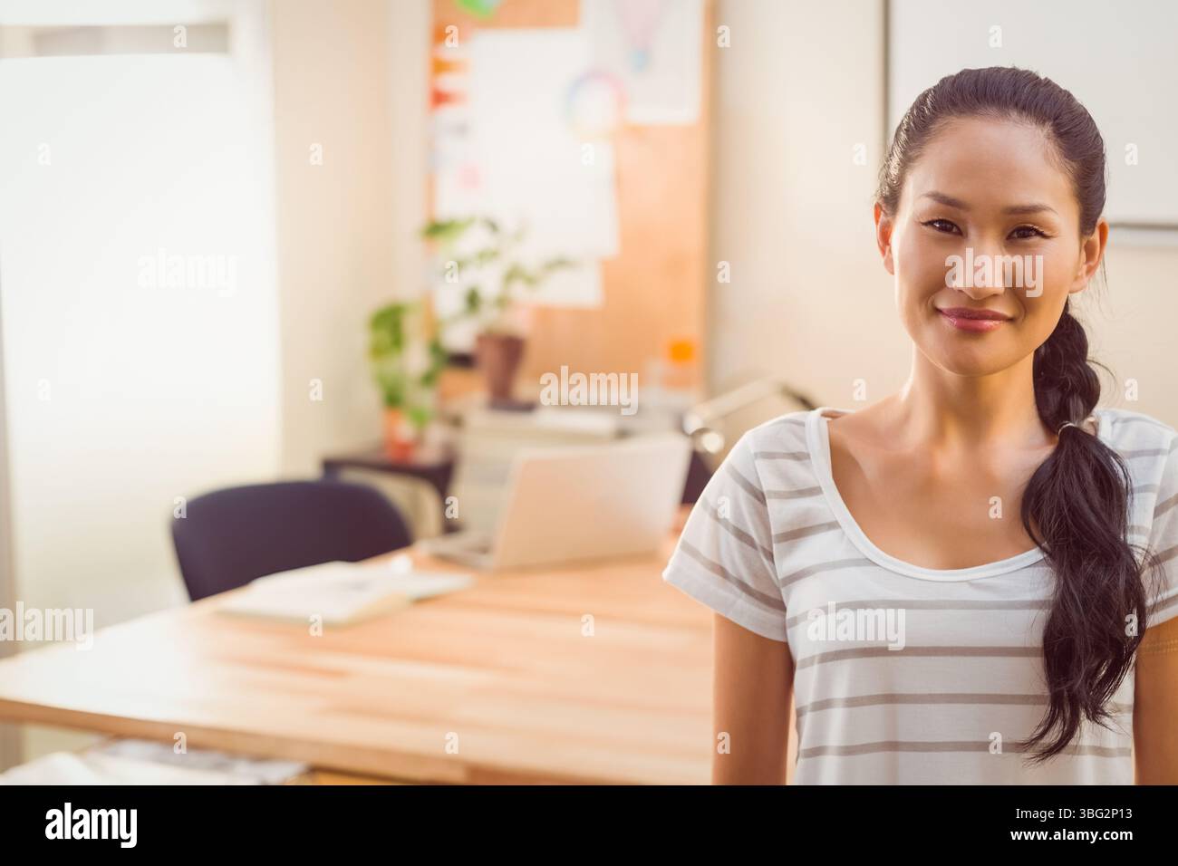 Asiatische Frau, die am Holzschreibtisch in hellem Arbeitsbereich mit offenem Laptop und Notizbüchern steht, Kopierraum Stockfoto