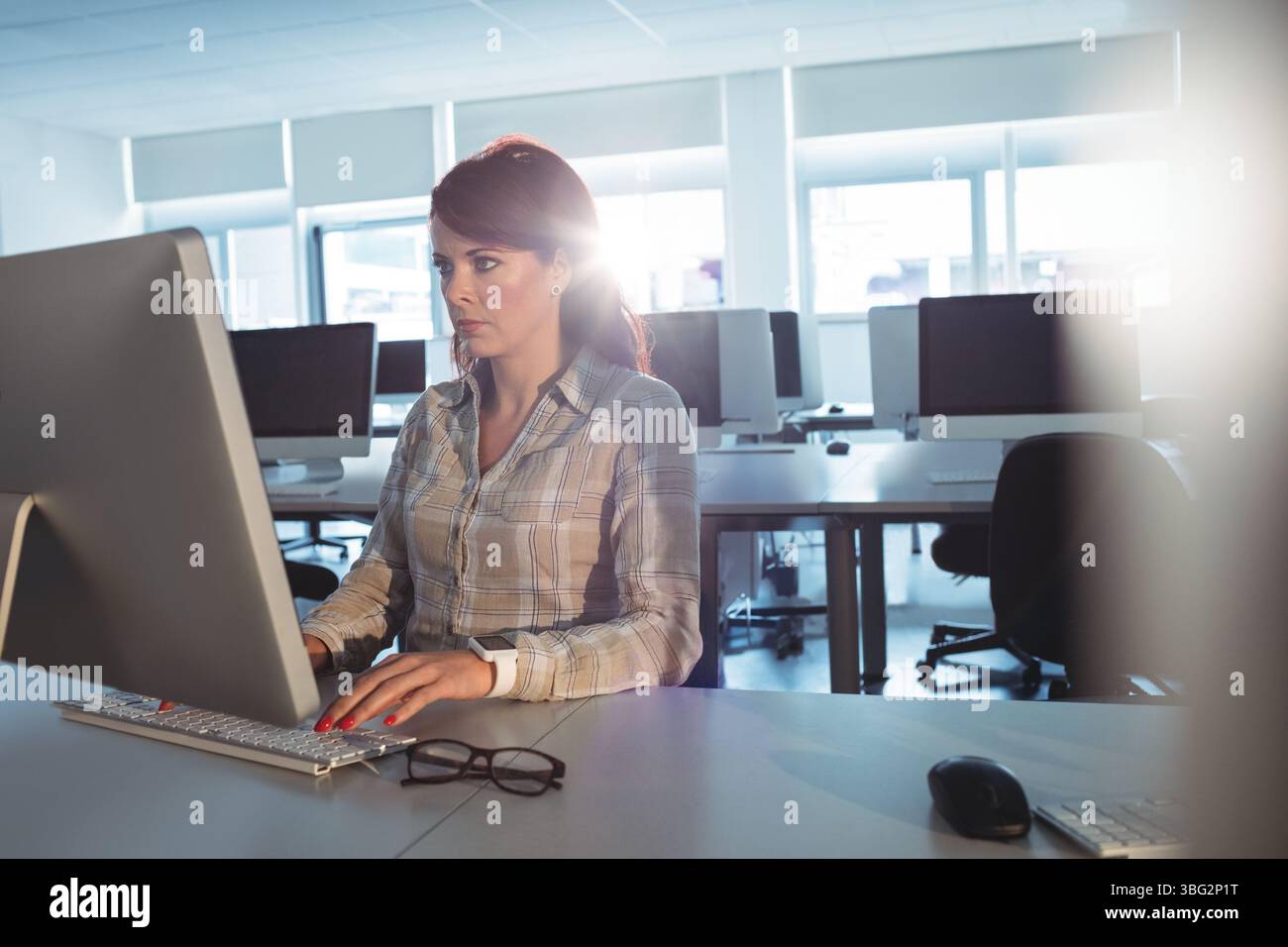Frau, die Tastatur und Maus am Schreibtisch im Computerlabor mit Monitor und Brille verwendet Stockfoto