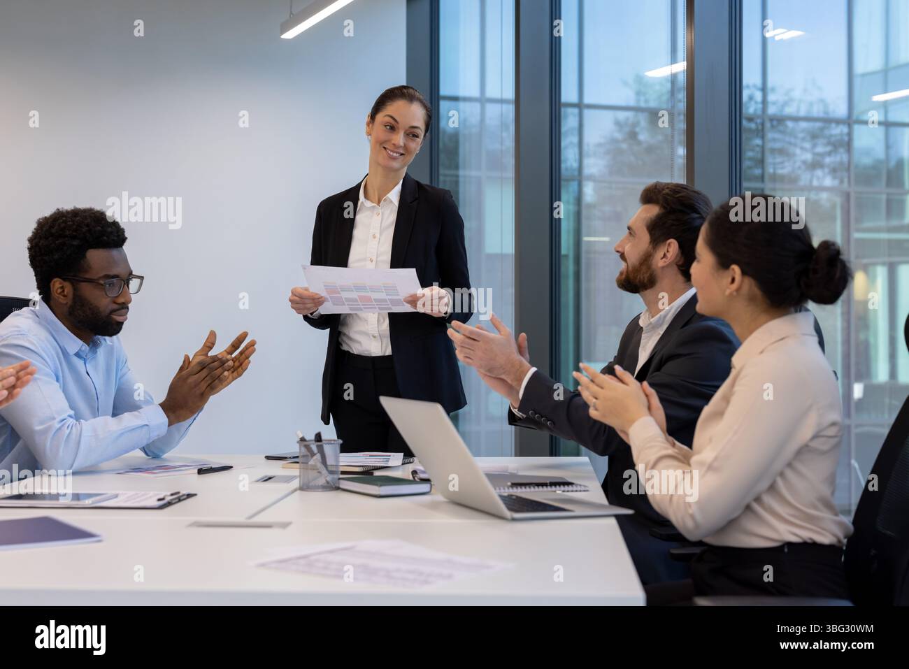 Eine Geschäftsfrau präsentiert sich während eines Meetings, während ihre Kollegen ihre Anerkennung für ihren Beitrag zum Team klatschen. Sie feiern den Erfolg. Stockfoto