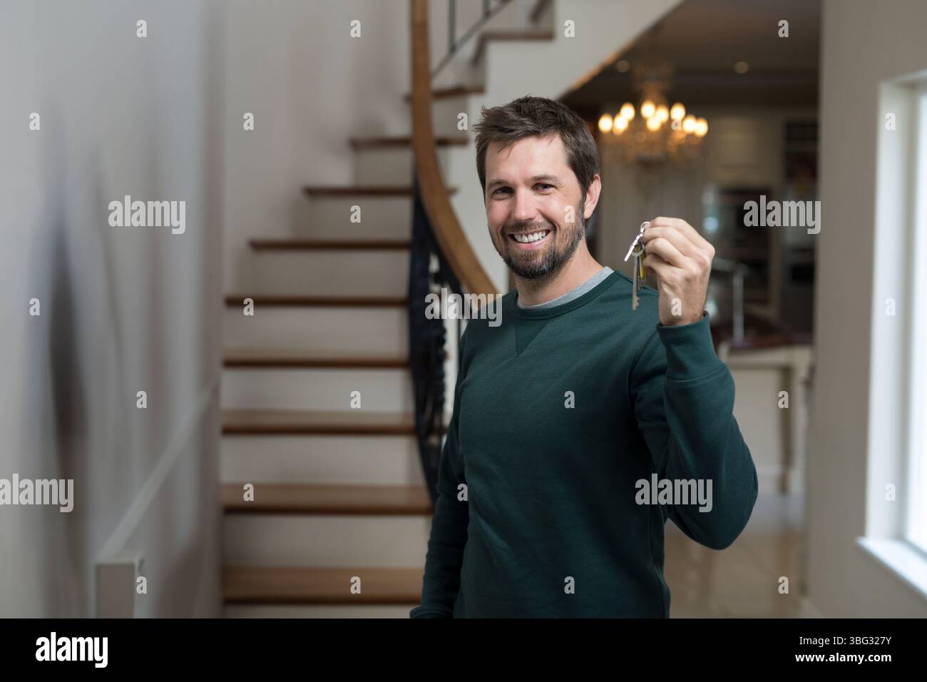 Bärtiger Mann, der unten auf einer Holztreppe im Wohneingang steht und den Schlüsselring hält Stockfoto