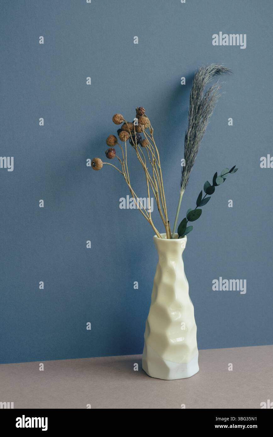 Vase mit trockener Blume auf dem Tisch. marineblauer Wandhintergrund Stockfoto