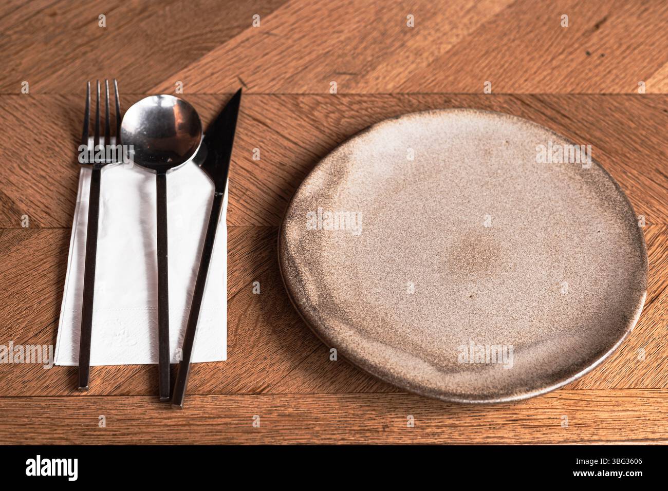 Besteck und ein einfacher, rustikaler Teller sind ordentlich auf einem Holztisch angeordnet und können zum Essen serviert werden. Stockfoto