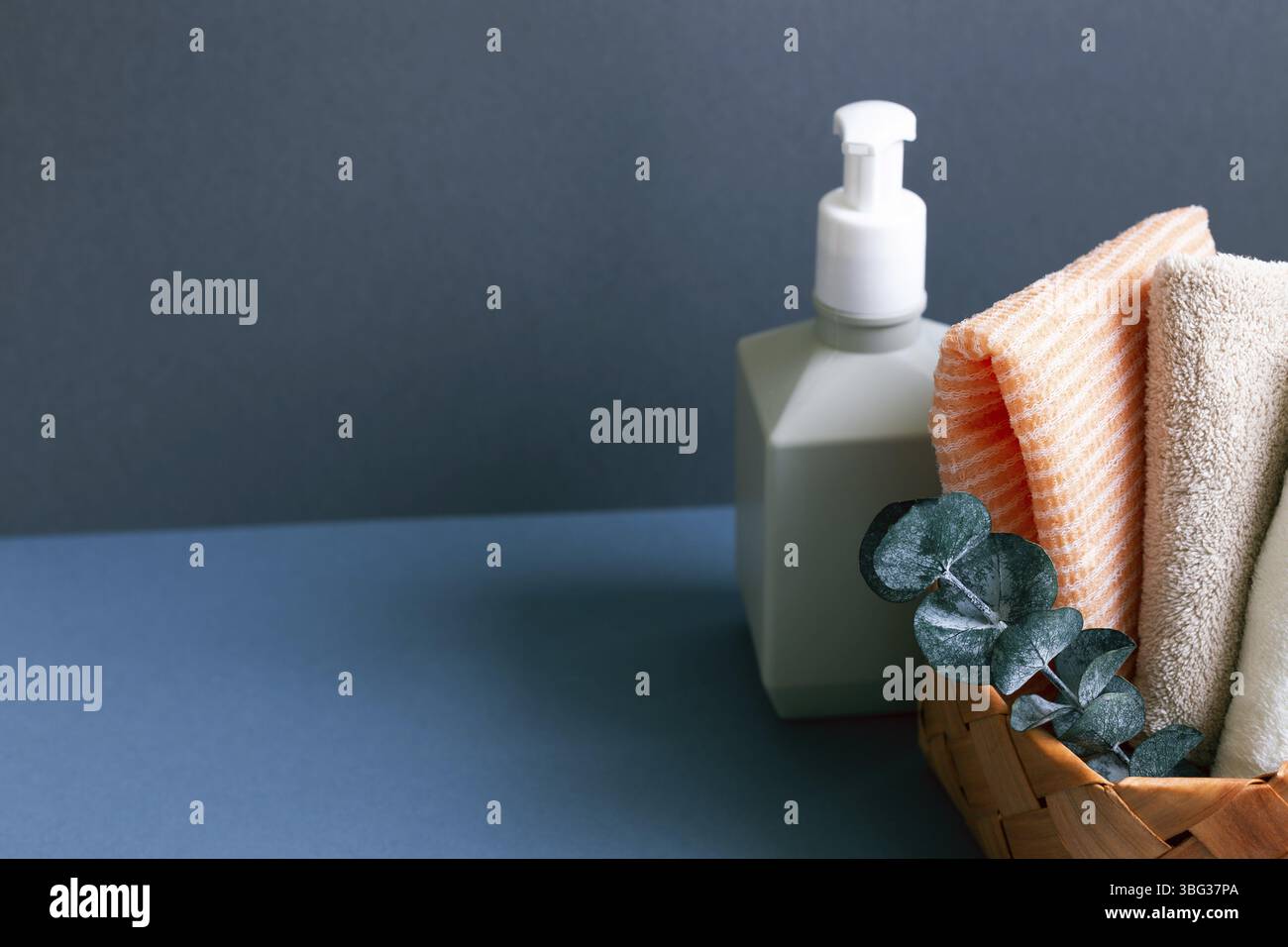 Seifenspender und Badetuch im Korb auf dem Tisch. marineblauer Wandhintergrund Stockfoto