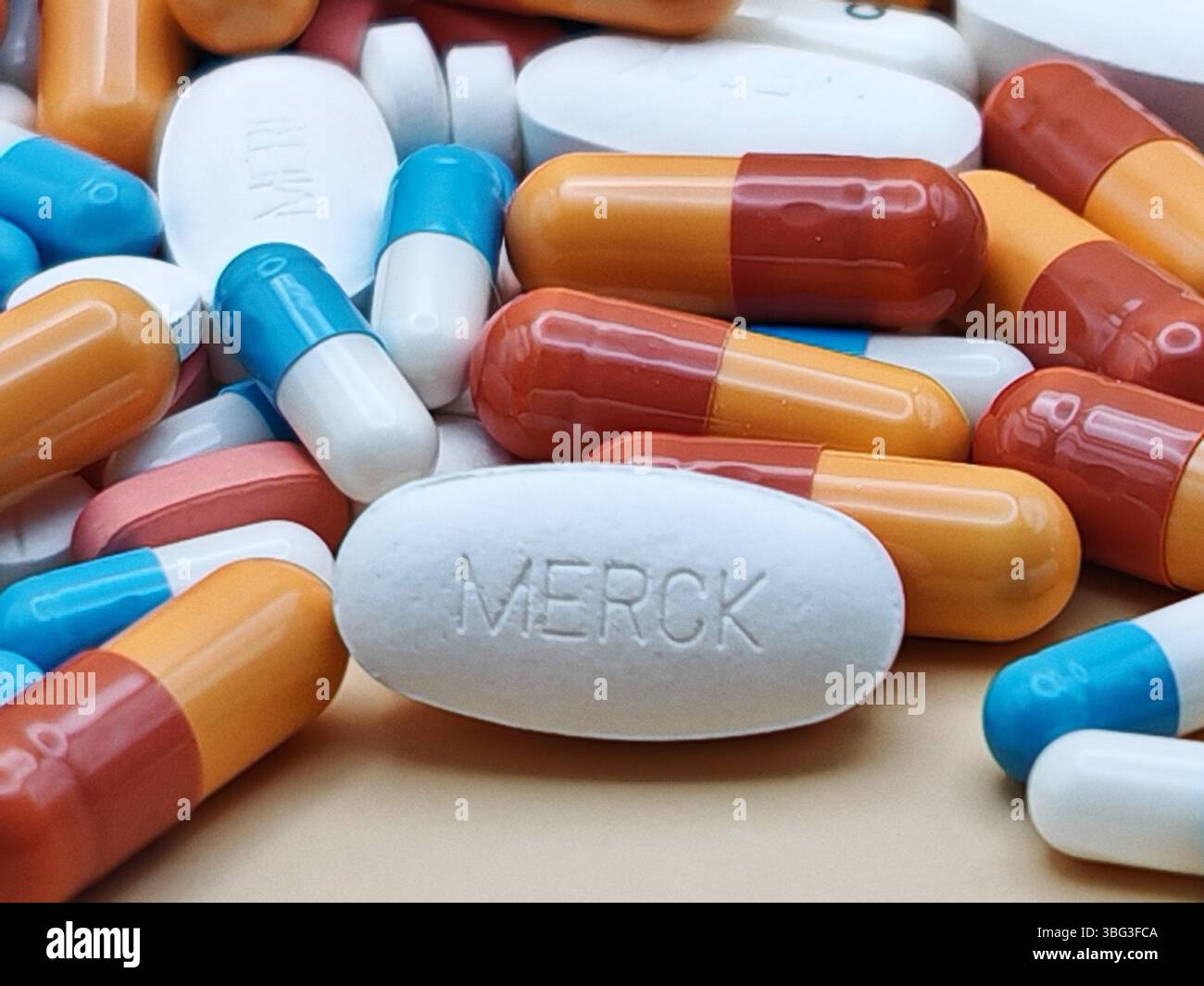 Weiße Pille mit MERCK-Aufdruck auf Tablettenstapel und farbenfrohe Kapseln in pharmazeutischer Optik. Stockfoto