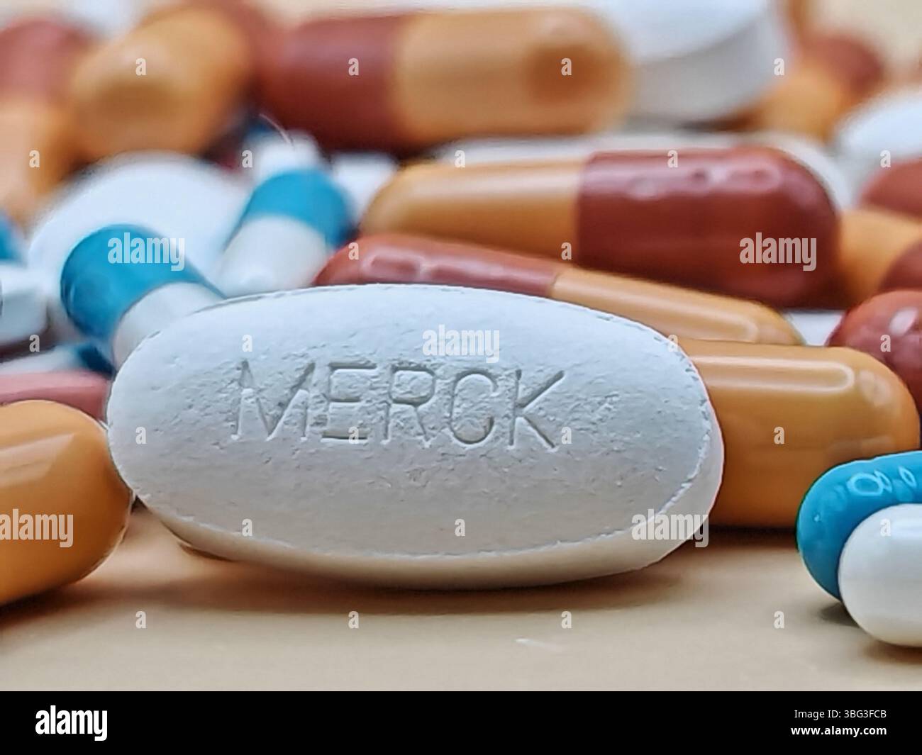 Weiße Pille mit MERCK-Aufdruck auf Tablettenstapel und farbenfrohe Kapseln in pharmazeutischer Optik. Stockfoto