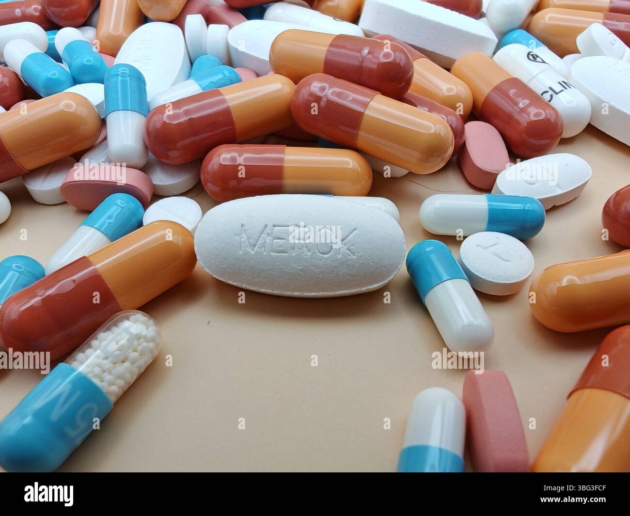 Weiße Pille mit MERCK-Aufdruck auf Tablettenstapel und farbenfrohe Kapseln in pharmazeutischer Optik. Stockfoto