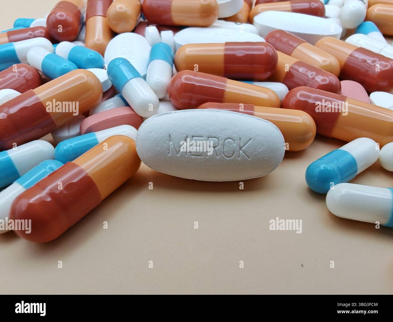 Weiße Pille mit MERCK-Aufdruck auf Tablettenstapel und farbenfrohe Kapseln in pharmazeutischer Optik. Stockfoto