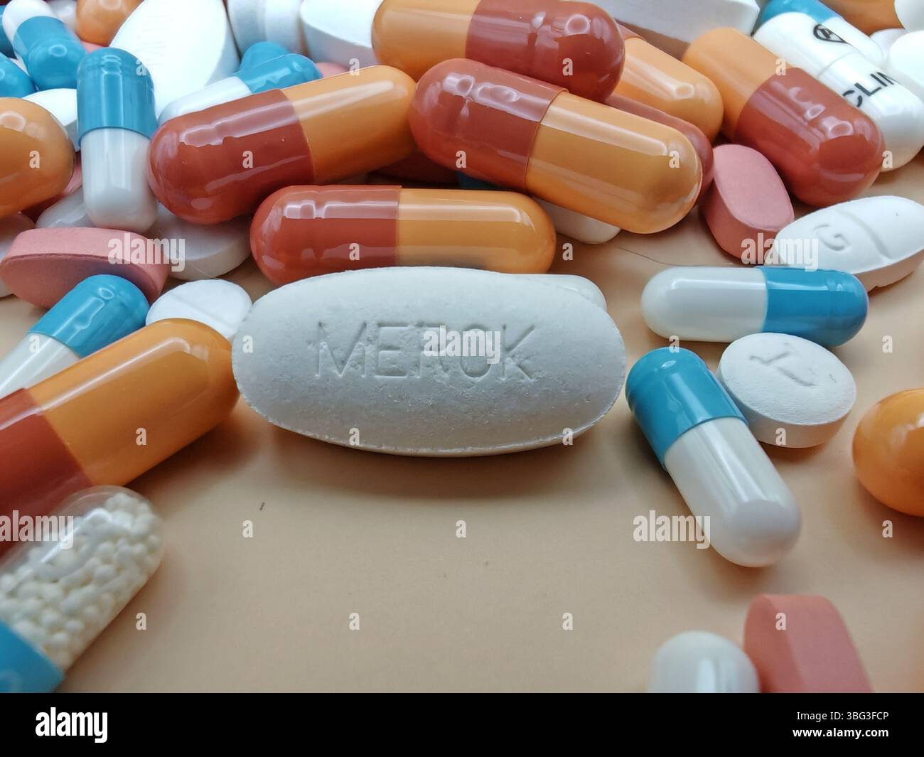 Weiße Pille mit MERCK-Aufdruck auf Tablettenstapel und farbenfrohe Kapseln in pharmazeutischer Optik. Stockfoto