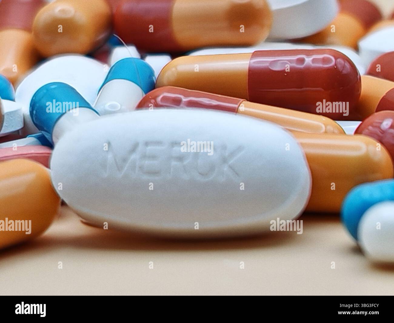 Weiße Pille mit MERCK-Aufdruck auf Tablettenstapel und farbenfrohe Kapseln in pharmazeutischer Optik. Stockfoto