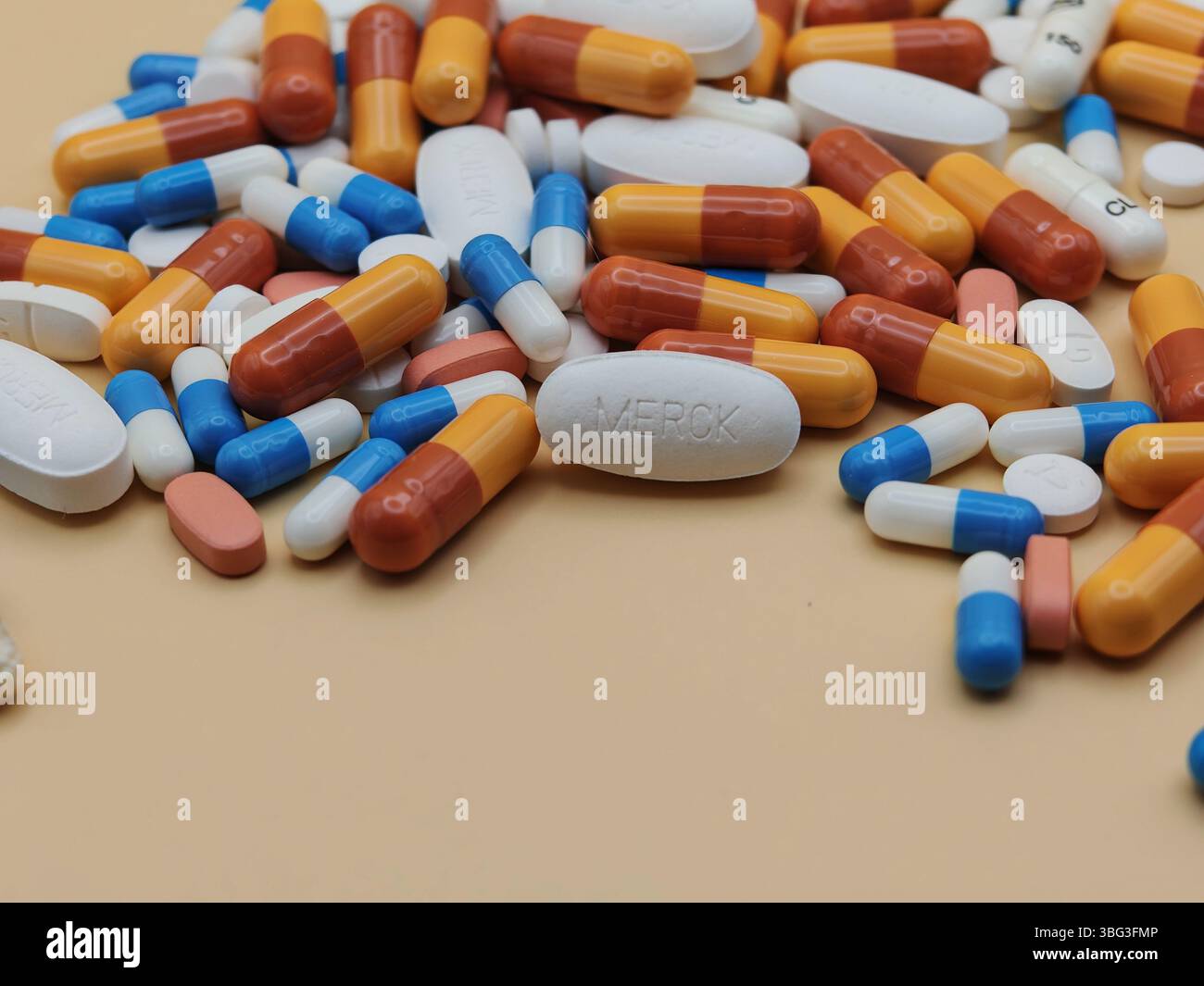 Weiße Pille mit MERCK-Aufdruck auf Tablettenstapel und farbenfrohe Kapseln in pharmazeutischer Optik. Stockfoto