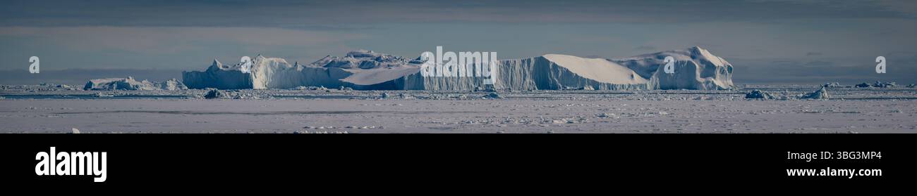 Dramatischer Blick auf schwimmende Eisberge in der Nähe von Disko Island, Grönland, mit bergiger Kulisse unter weichem Polarlicht. Stockfoto