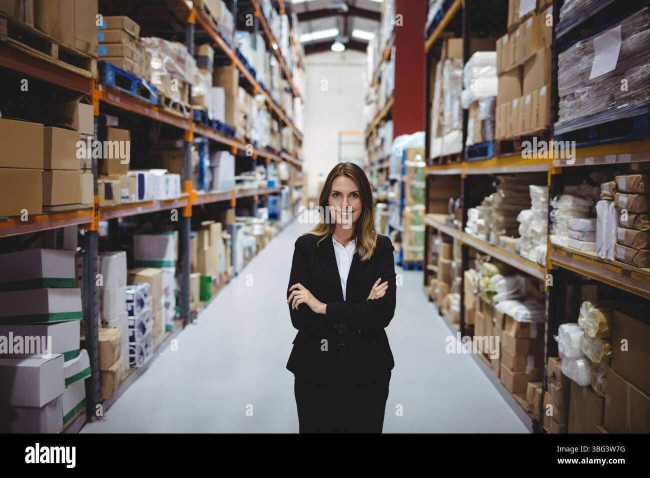 Geschäftsfrau, die Lagerbestände im Lagerhaus mit Metallregalen und Paletten inspiziert Stockfoto