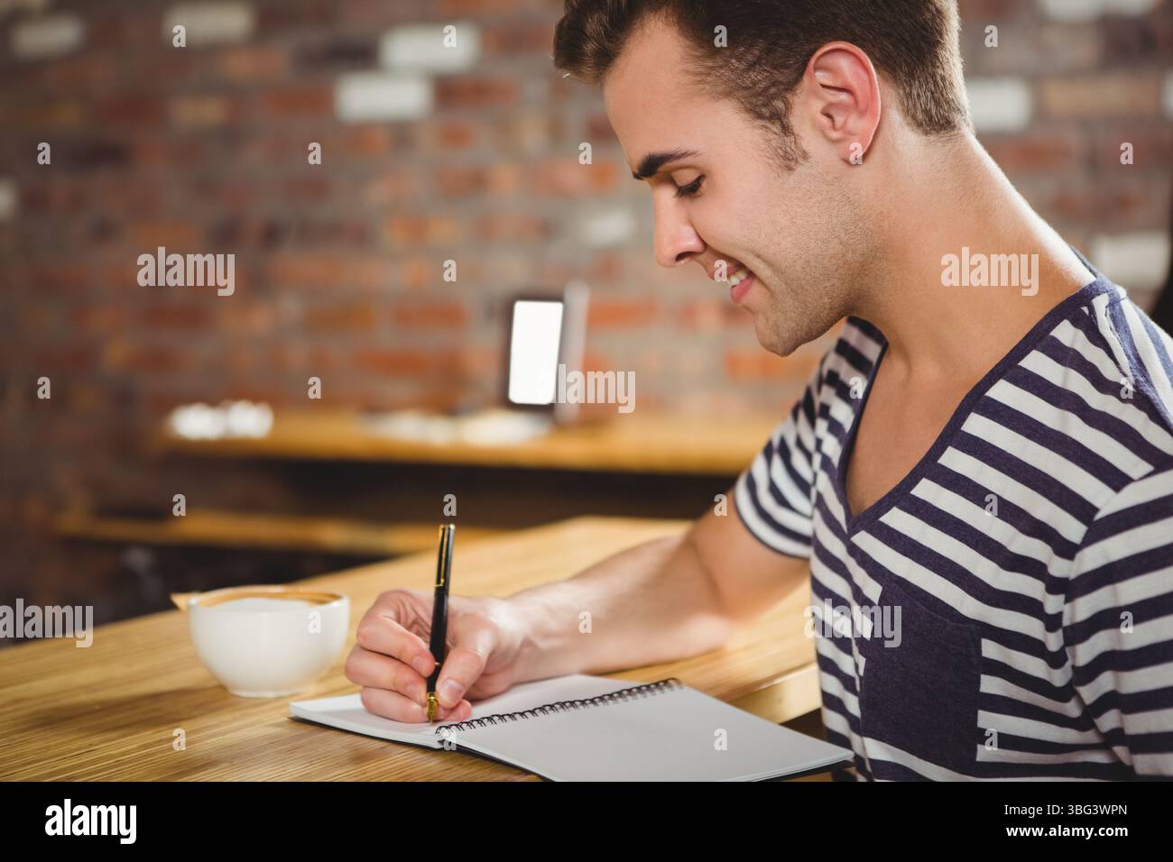 Mann, der in Notizbuch mit Stift an gemauerten Kaffeetisch mit Kaffeetasse, Kopierraum schreibt Stockfoto