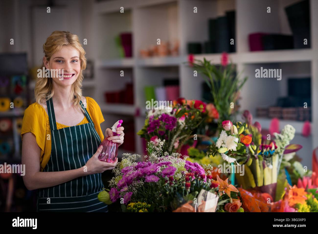 Blumenhändler sprühen Wassernebel auf leuchtende Blumensträuße am Ladentisch und zeigen farbenfrohe Ausstellungspunkte Stockfoto