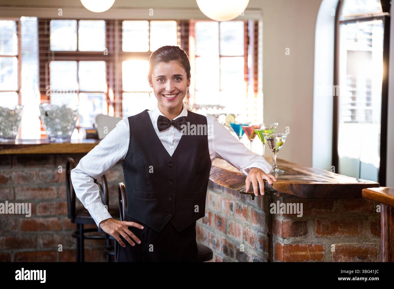 Weibliche Barkeeperin in Uniform, die an der Backsteintheke bunte Cocktails anbietet Stockfoto