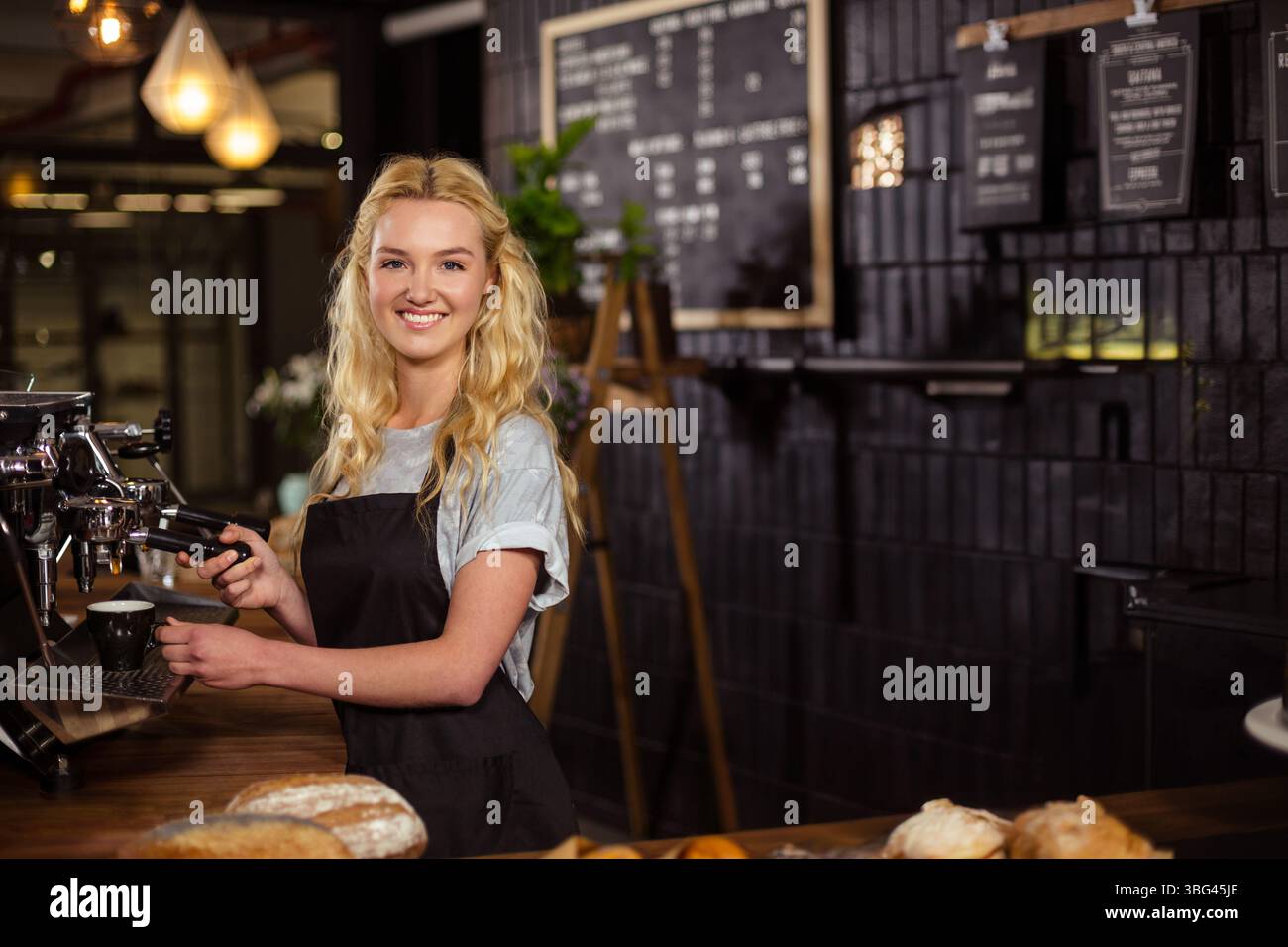 Lächelnde Barista, die am Ladentisch eine Kaffeetasse auf der Espressomaschine mit Portafilter füllt Stockfoto