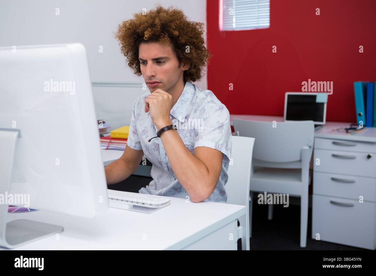 Männlicher Büroangestellter sitzt am Schreibtisch in einem modernen Büro und starrt auf den Monitor zwischen Tastatur und Maus Stockfoto