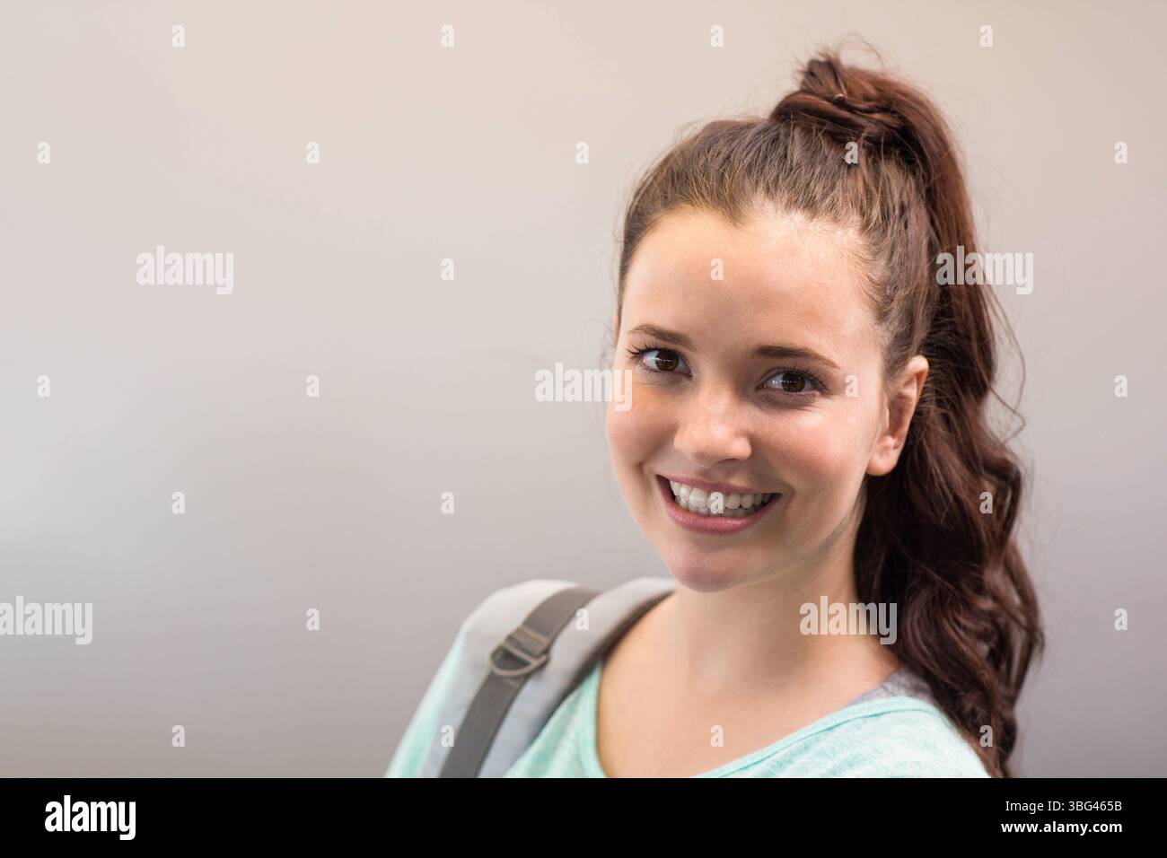 Studentin, die im Flur steht, trägt mintgrüne Oberseite und grauen Rucksackriemen, Kopierraum Stockfoto