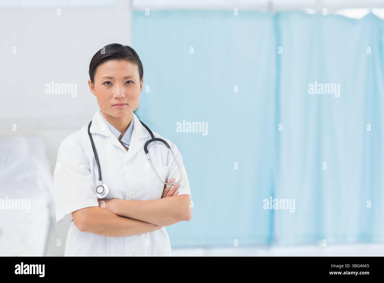Doktor mit weißem Mantel und Stethoskop, mit Armen, die von Untersuchungsbett überkreuzt werden, Privatvorhang Stockfoto
