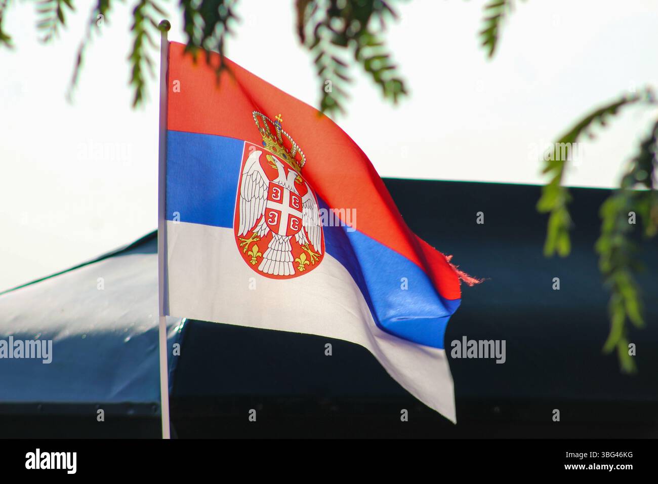 Novi Sad, Serbien – 14. Mai 2025: Die serbische Flagge wird im Freien gefangen genommen, während sie sich im Wind unter direktem Sonnenlicht bewegt. Stockfoto