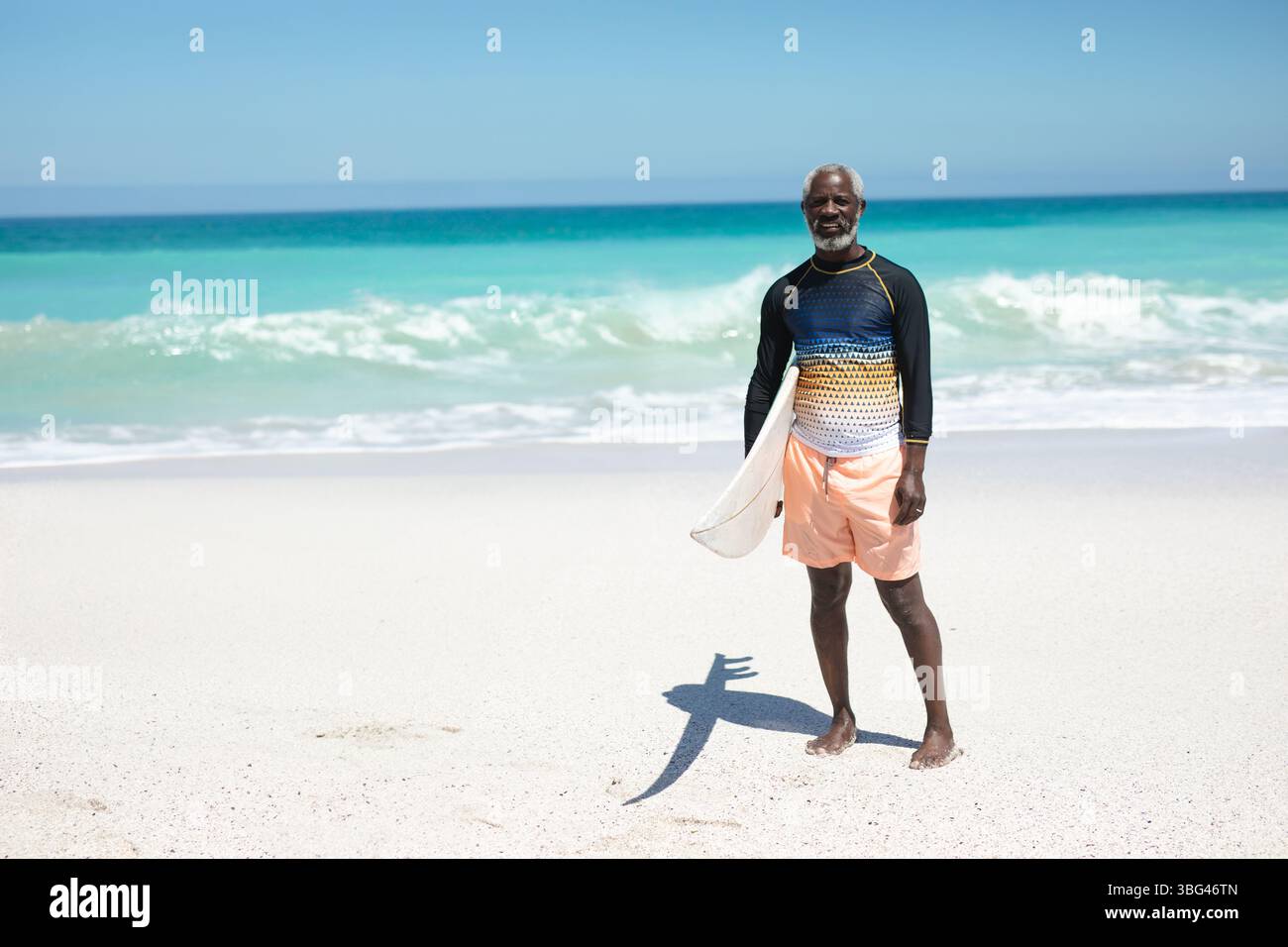 Afroamerikaner, der am Strand steht und ein Schwimmhemd trägt, Surfbrett hält, Kopierraum Stockfoto