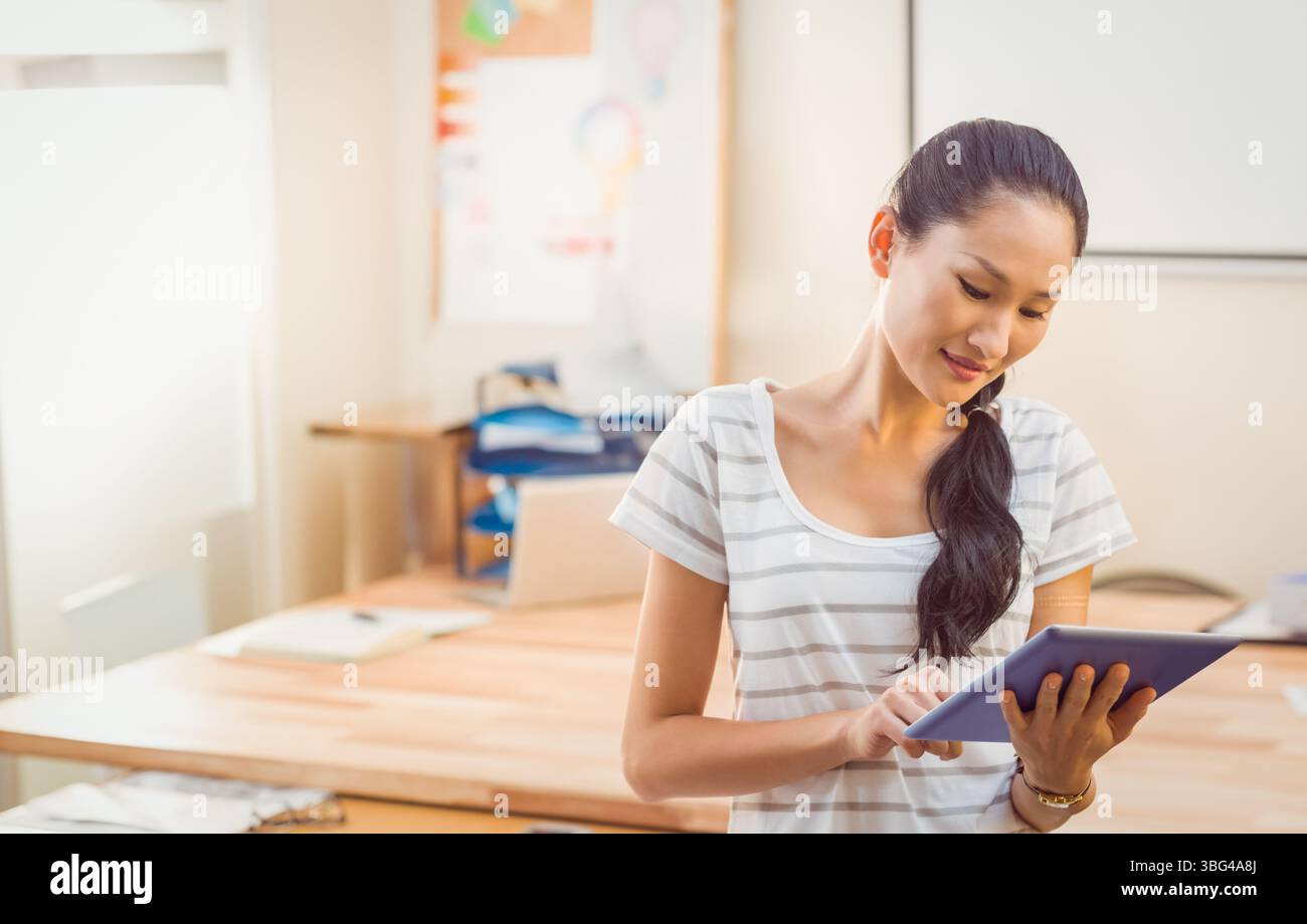 Asiatische Frau, die im Heimbüro steht und ein Tablet am Holzschreibtisch mit Laptop, Kopierraum antippt Stockfoto