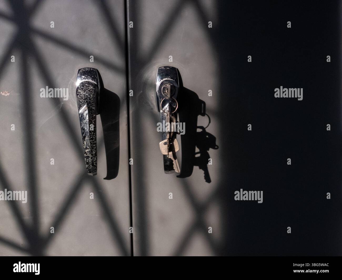 Nahaufnahme von zwei modernen Türgriffen mit einem Schlüssel. Das Spiel der Schatten erzeugt ein optisch eindrucksvolles Muster, das den Glanz des Metalls unterstreicht. Stockfoto