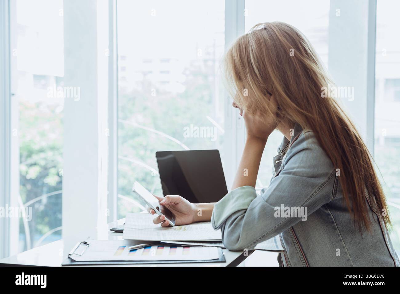 Junge Geschäftsfrauen spielen Smartphone, Handy am Schreibtisch, schauen sich soziale Medien an Stockfoto