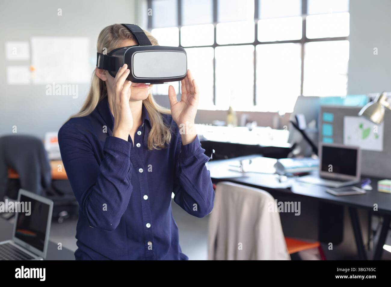 Virtual-Reality-Headset, das auf dem Schreibtisch zwischen Monitoren sitzt, Laptops, Papiere im hellen Großraumbüro Stockfoto