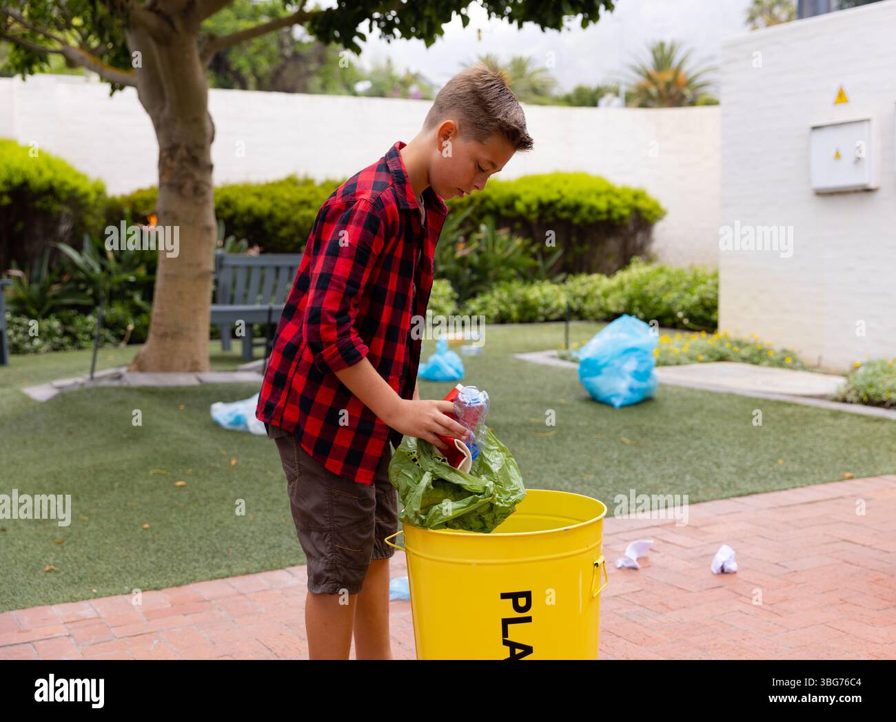 Kunststoffflaschen und grüne wiederverwendbare Beutel werden in gelben Recyclingbehälter auf der Terrasse gelegt Stockfoto